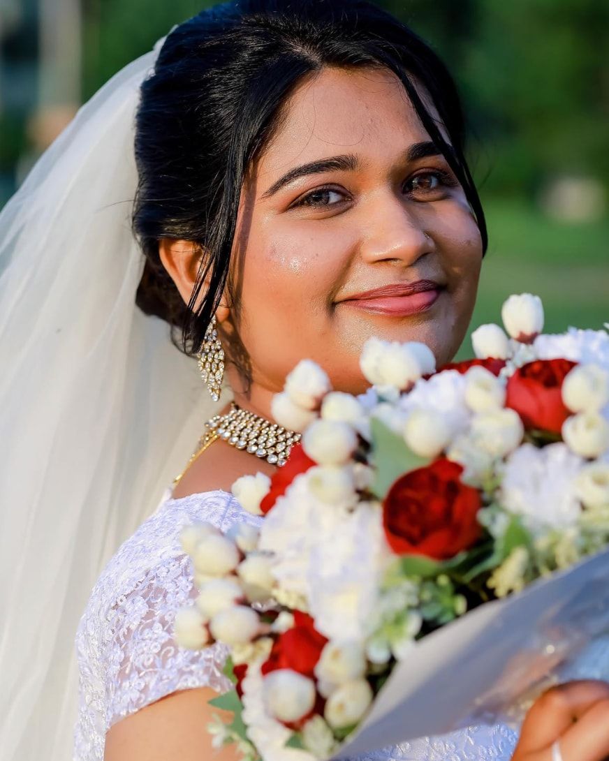 Smiling bride in a white veil holding a red and white bouquet